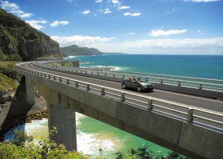 Long view of car driving along Sea Cliff Bridge, Grand Pacific Drive, with coastal views in background, Illawarra