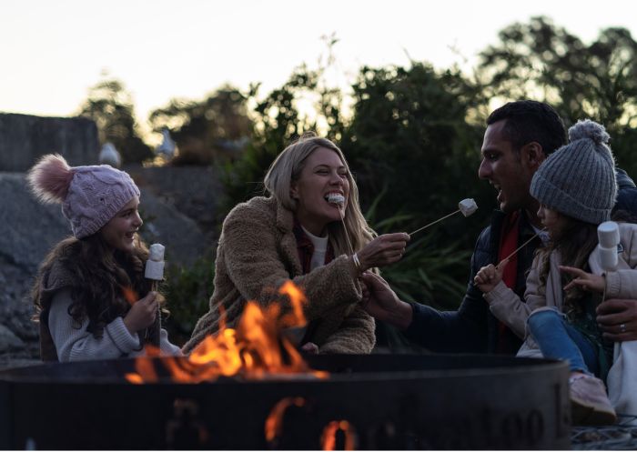 Family relaxing and roasting marshmallows at their Cockatoo Island waterfront campsite