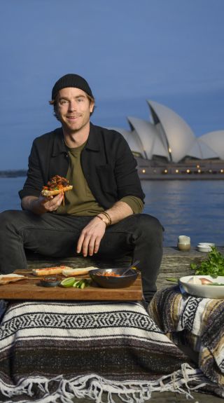 Hayden Quinn cooking Lemongrass Pork Roll with Opera House in background, Sydney Harbour