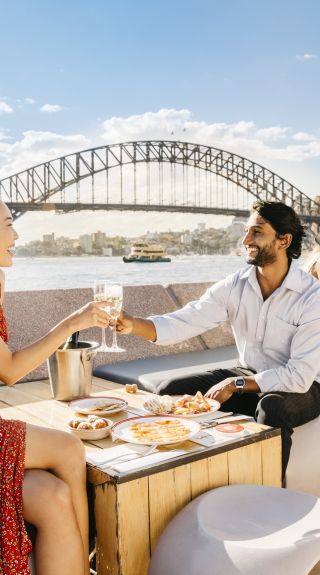 Couple enjoying food and drink with harbour views at Opera Bar, Sydney.